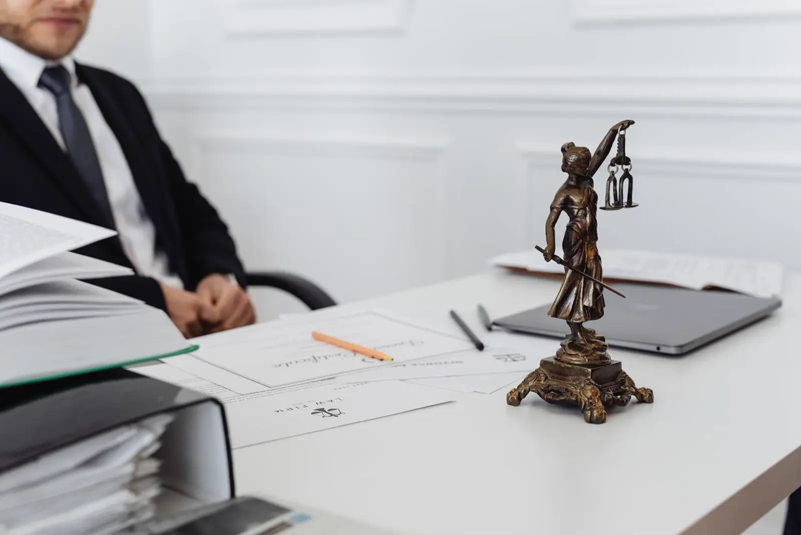 A legal desk with documents, a laptop and a scales of justice statue