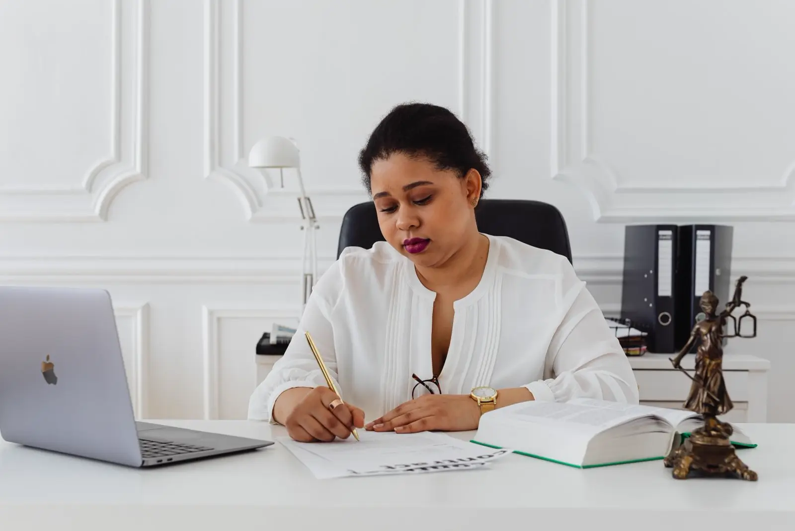 A professional woman signing papers at a desk beside a laptop and a law book