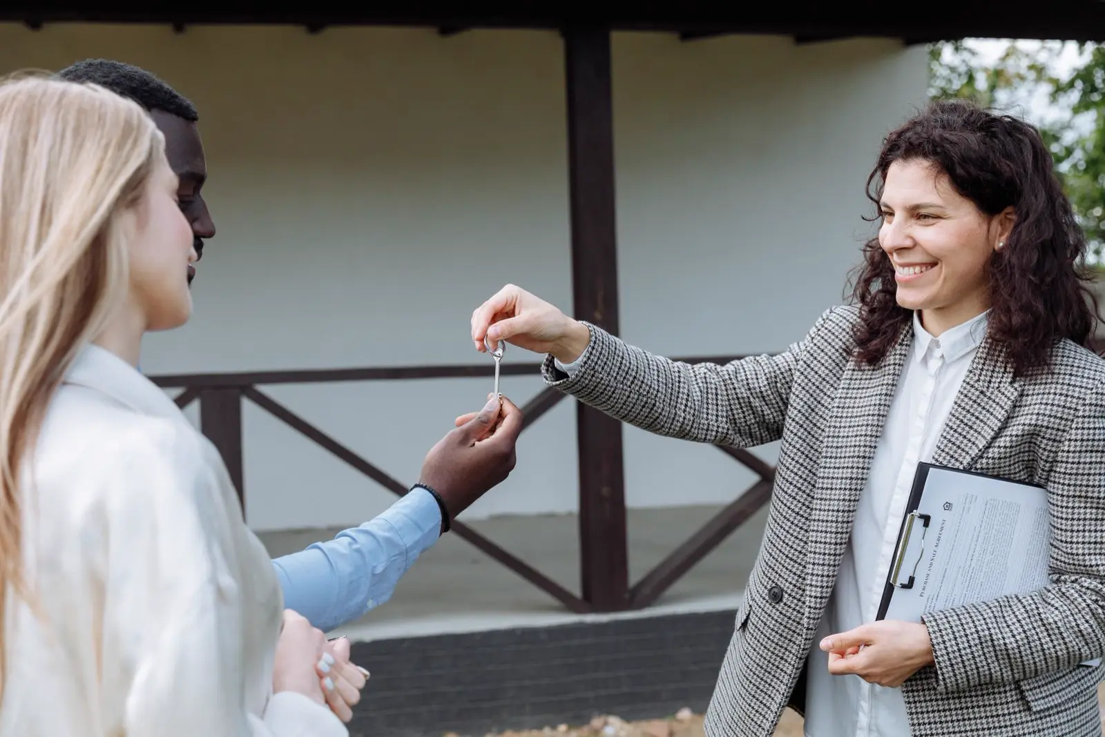A real estate agent handing keys to a couple outside their new home