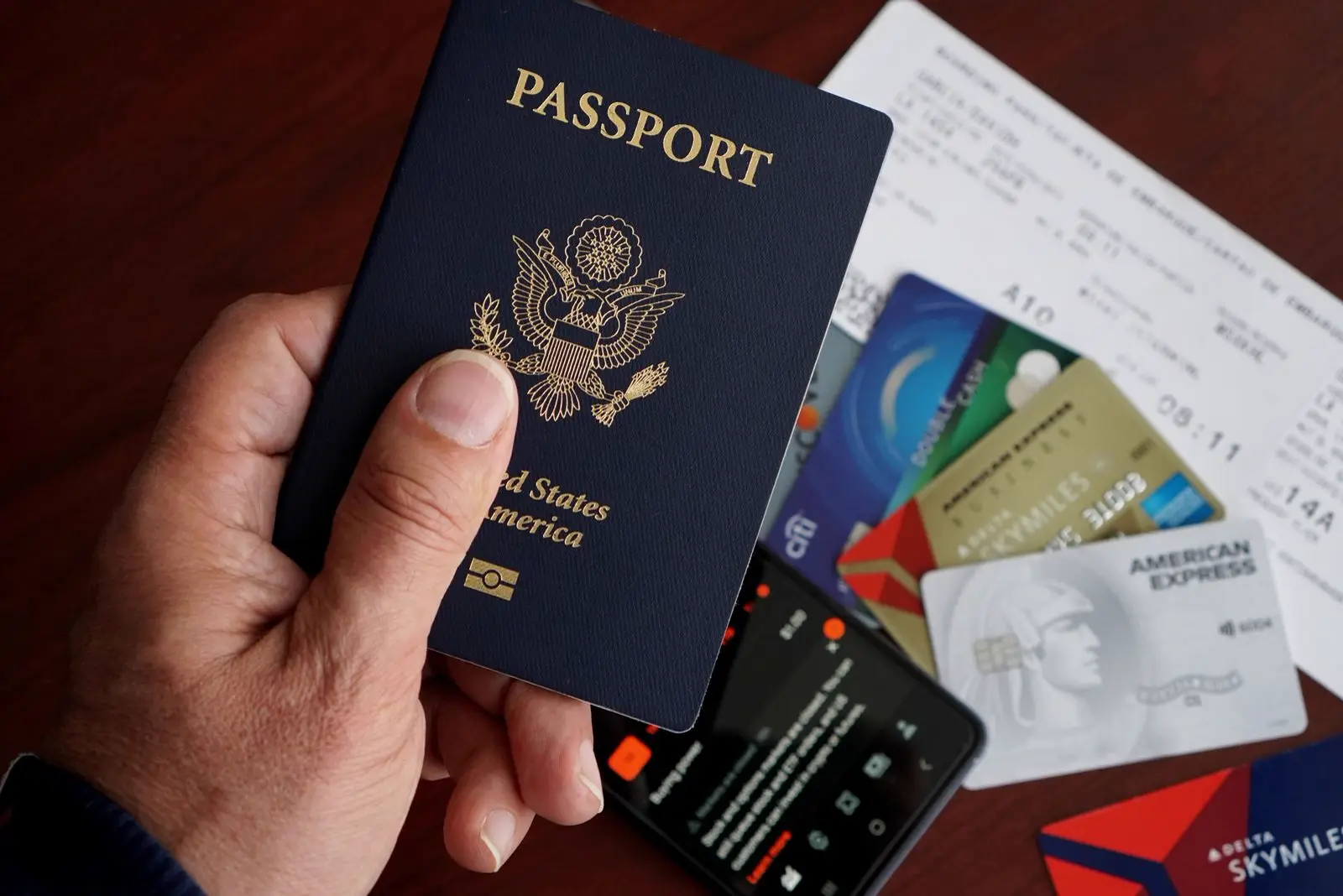 A hand holding a U.S. passport with travel documents and cards