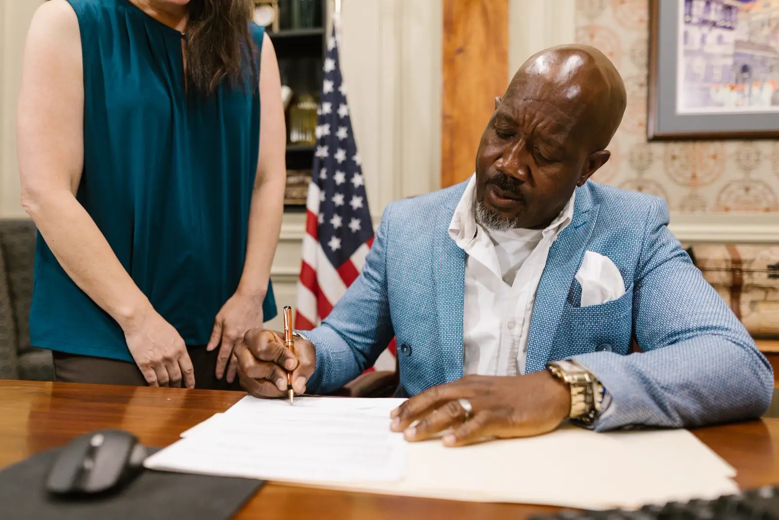 A signer at his desk in front of an American flag, signing a document